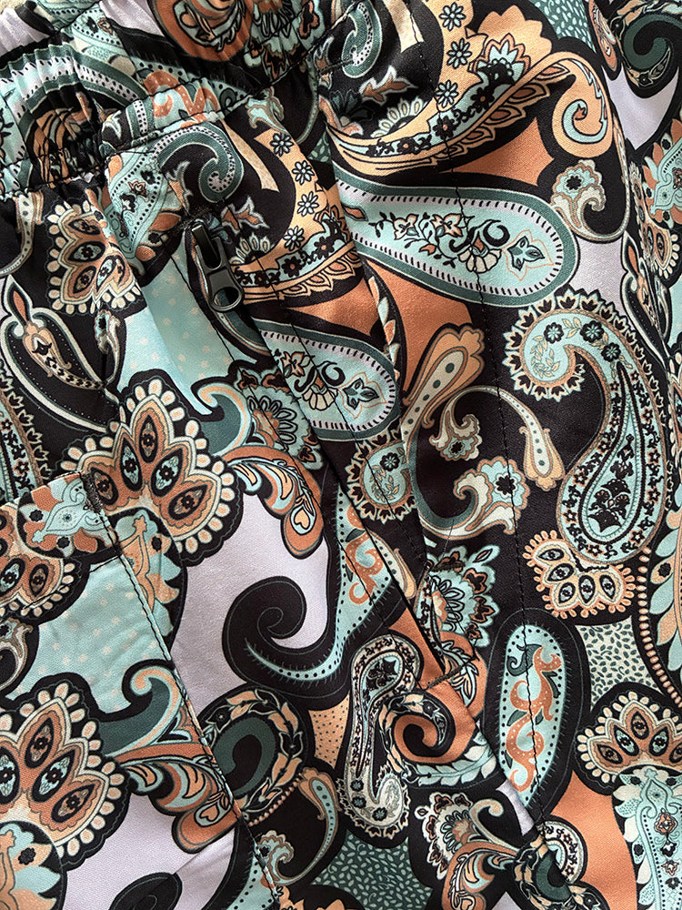 A close-up of a paisley fabric with a black base and intricate patterns in teal, peach, beige, and white.
