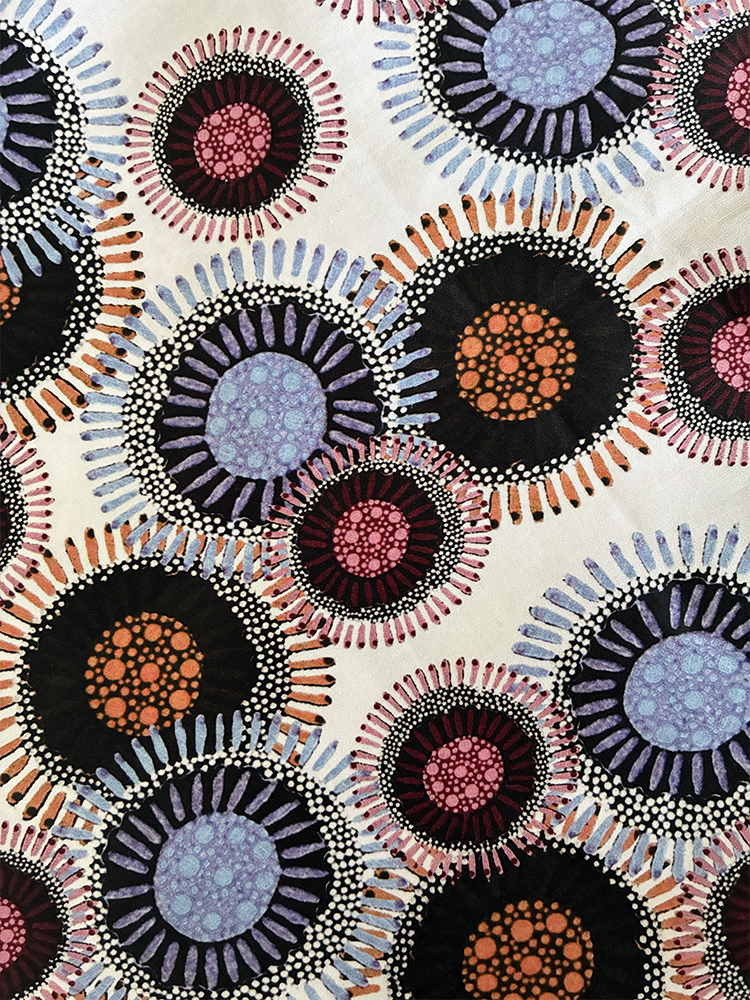A close-up of a shirt pattern featuring overlapping circular motifs in black, purple, pink, orange, and light blue on a cream background.