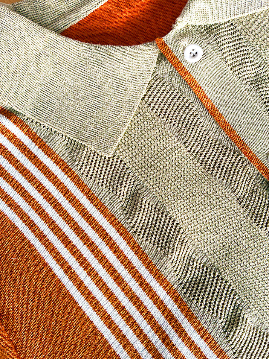 Close-up of a knit polo shirt showing a light beige collar, textured knit body, orange contrast stitching, and orange-and-white striped sleeve detail.