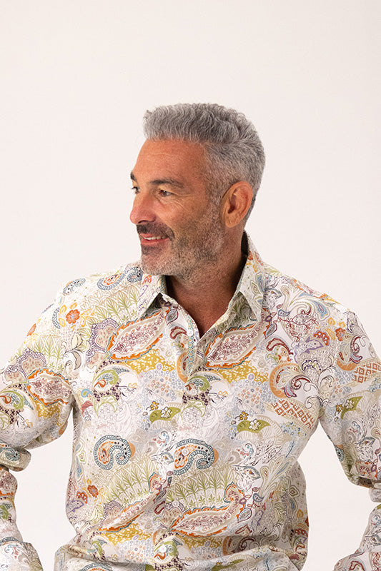 Man with grey hair wearing a paisley pattern shirt in beige.
