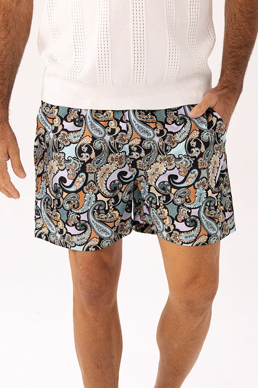 Men's patterned shorts featuring a intricate paisley design in black, teal, orange, and white, styled with a white knit top against a plain white background.