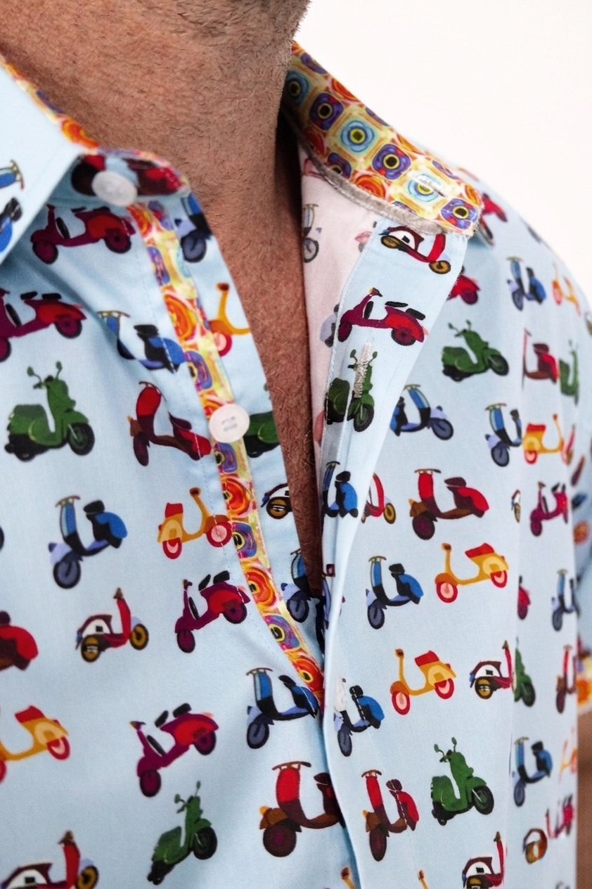 A close-up of a light blue button-down shirt featuring a colorful retro scooter print, worn by a man.