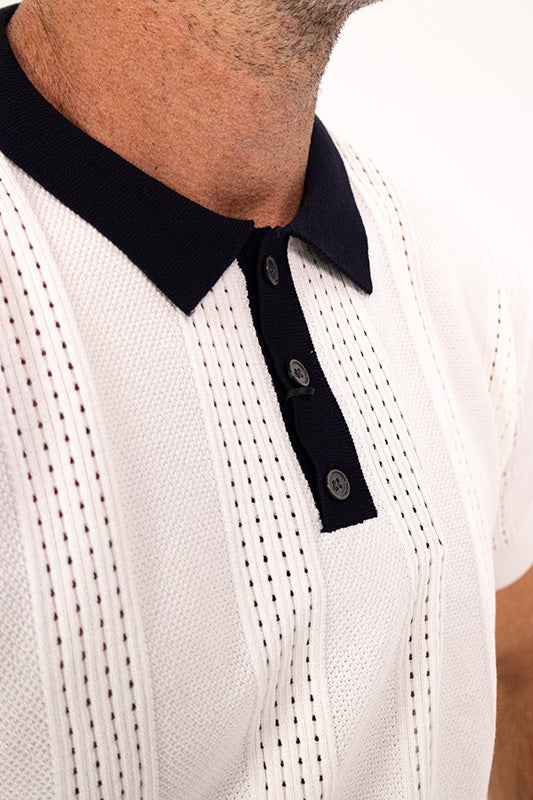 Close-up of a man wearing a white knit polo shirt with vertical dotted stripe patterns and a contrasting dark navy collar and button placket.