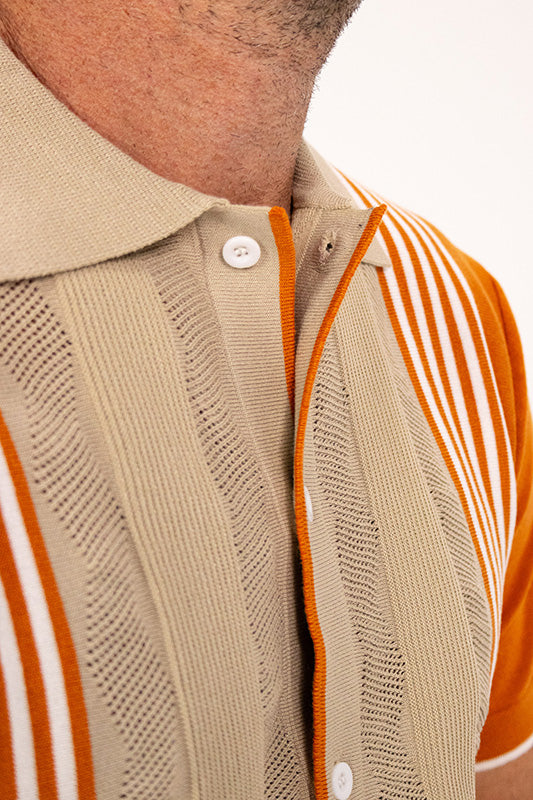 Close-up of a beige knit polo shirt with orange and white striped sleeves and collar trim, worn by a model.