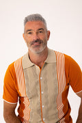 A man with gray hair and a beard wearing a retro-style short-sleeve button-up shirt with orange and beige wavy vertical stripes, photographed against a plain white background.