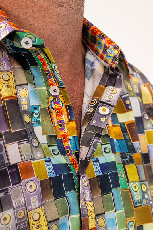 A close-up of a person wearing a short-sleeve button-up shirt with a vibrant retro cassette tape pattern in multiple colors including blue, yellow, green, orange, and purple.