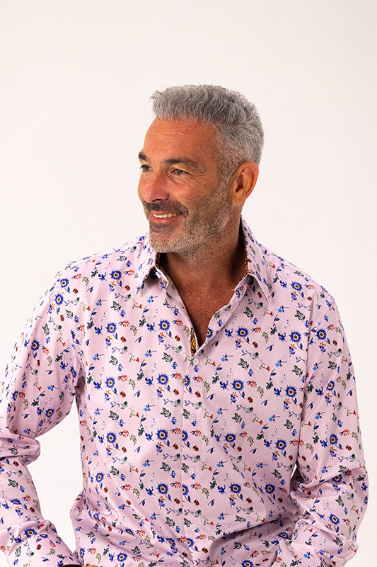 A man with gray hair and a beard wearing a light pink long-sleeve button-up shirt with a blue, red, and green floral print, photographed against a plain white background.