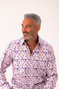 A man with gray hair and a beard wearing a light pink long-sleeve button-up shirt with a blue, red, and green floral print, photographed against a plain white background.