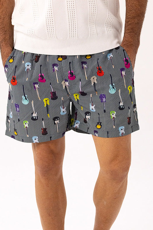 A person wearing patterned shorts with a gray and white vertical stripe base and colorful guitar illustrations, paired with a white knit top against a plain white background.