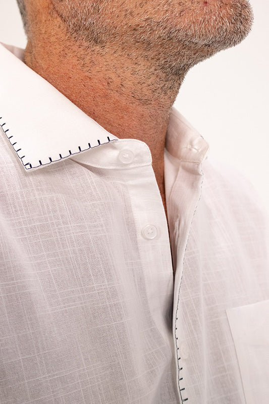 Close-up of a man wearing a white textured linen shirt with black contrast stitching along the collar and front placket.