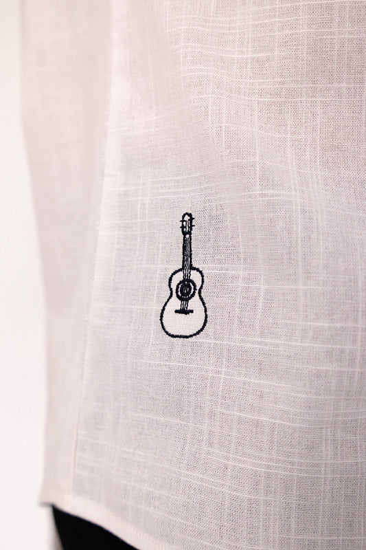 A close-up of a light beige linen fabric with a small black embroidered acoustic guitar motif in the center.