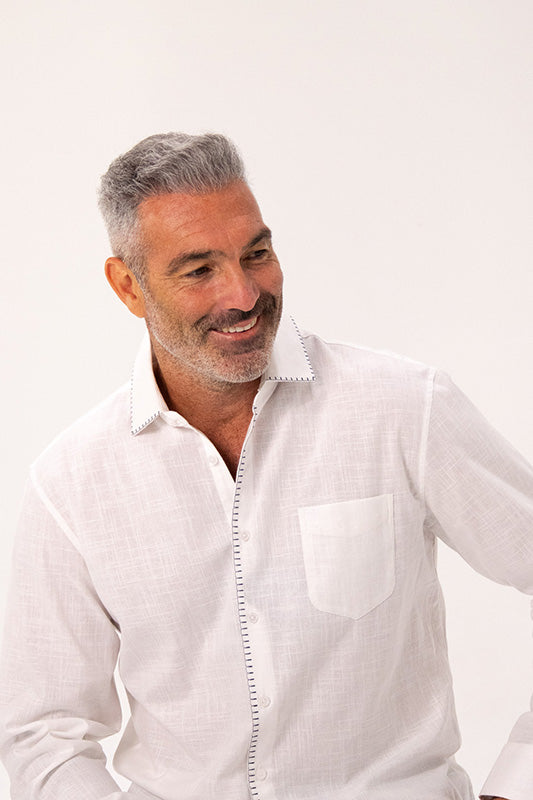 A smiling man with gray hair wearing a white textured linen button-down shirt with a pointed collar and a chest pocket, set against a plain white background.