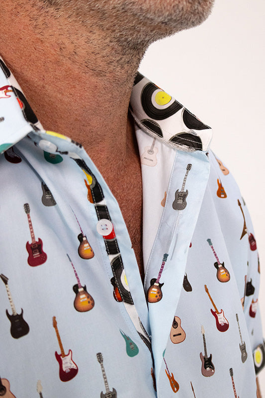 Close-up of a man wearing a light blue button-up shirt with an all-over printed pattern of electric and acoustic guitars, with a white inner collar featuring a black and yellow circular design.