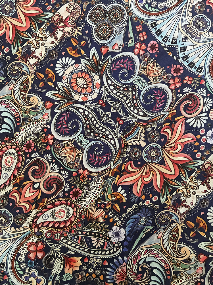 A close-up of a highly detailed, multicolor paisley and floral pattern on a dark navy blue background, featuring intricate hand-drawn style designs in red, orange, pink, beige, and white.